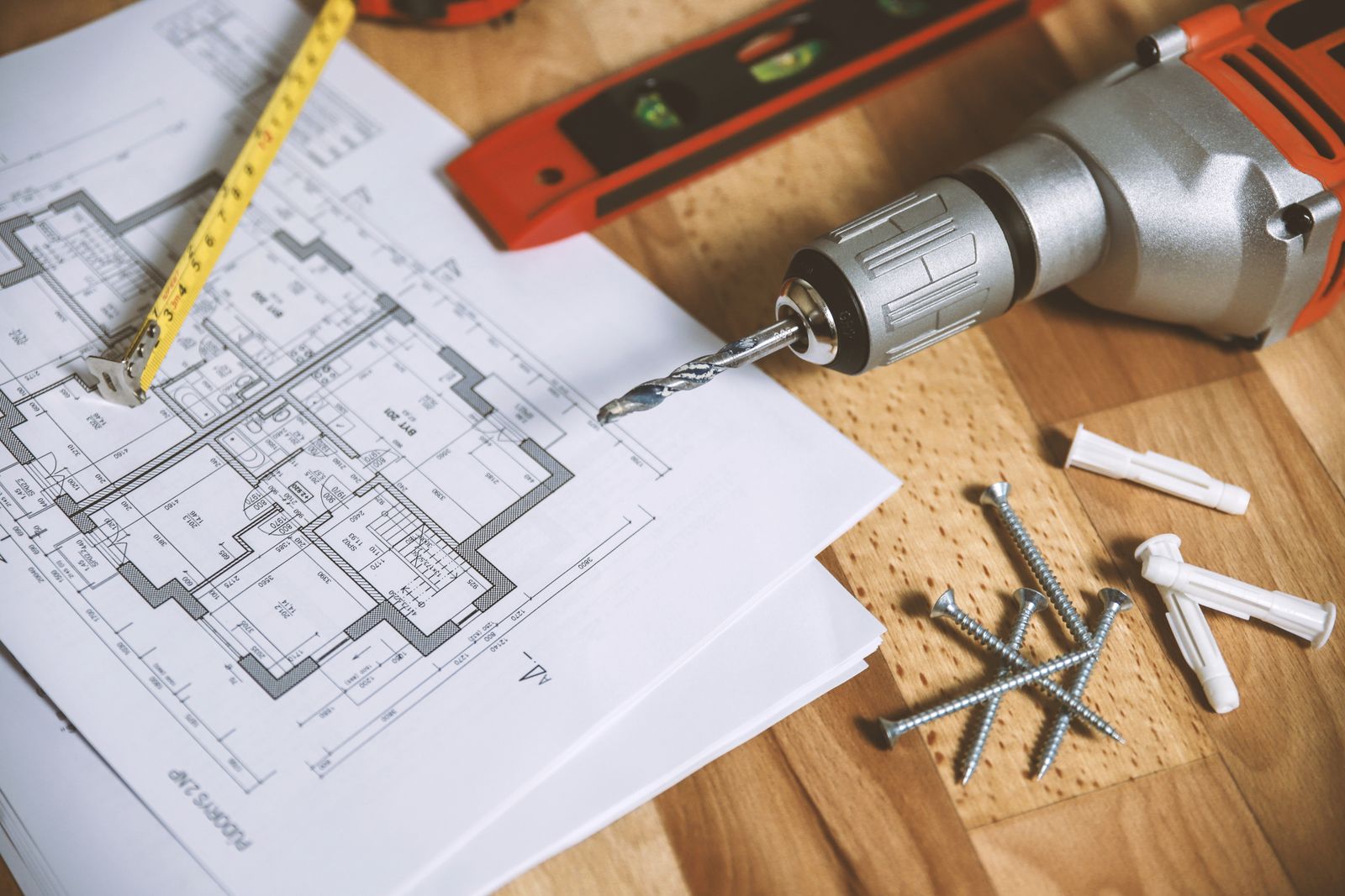 Printed plans on a wooden bench with a tape measure, a level, and a drill.